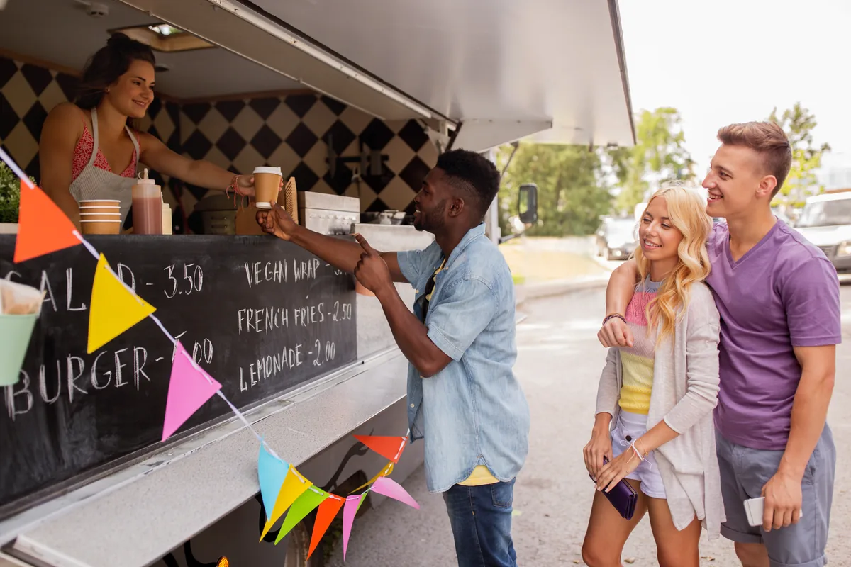 A food truck owner serving a drink to customers at the counter
